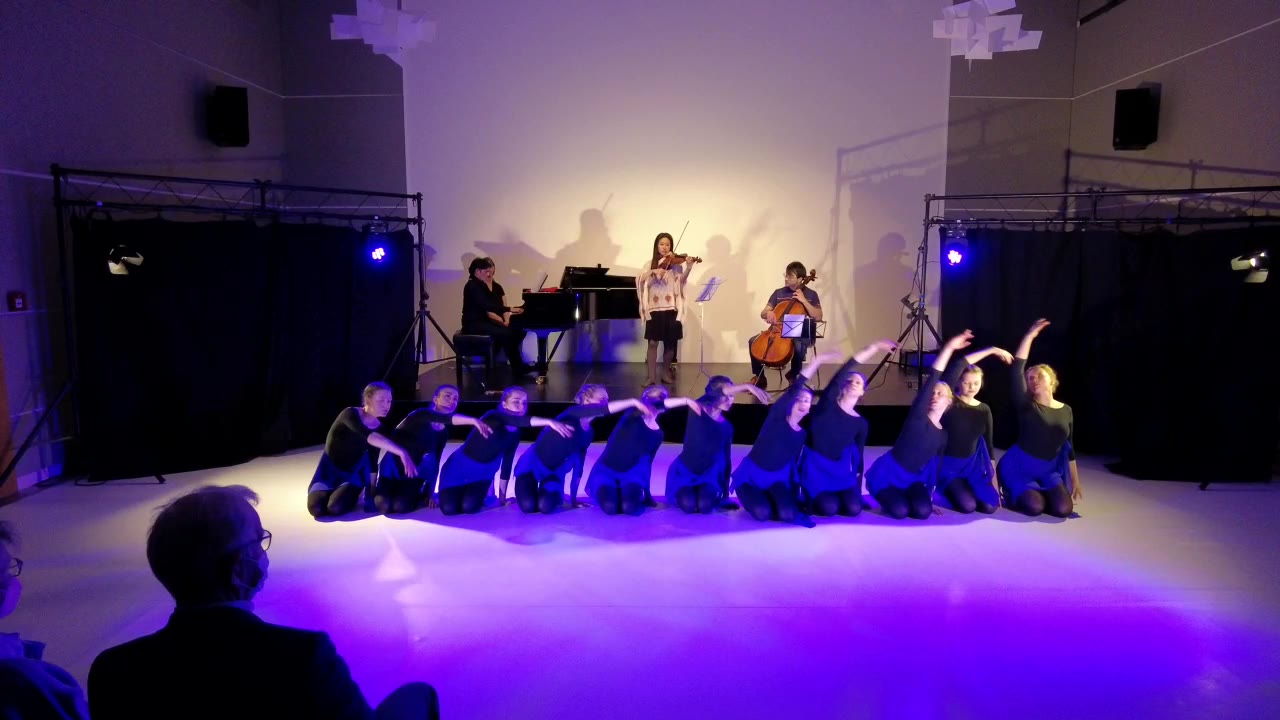 Das Ensemble kniet am Ende des Finales in violettem Licht, dahinter die Musiker